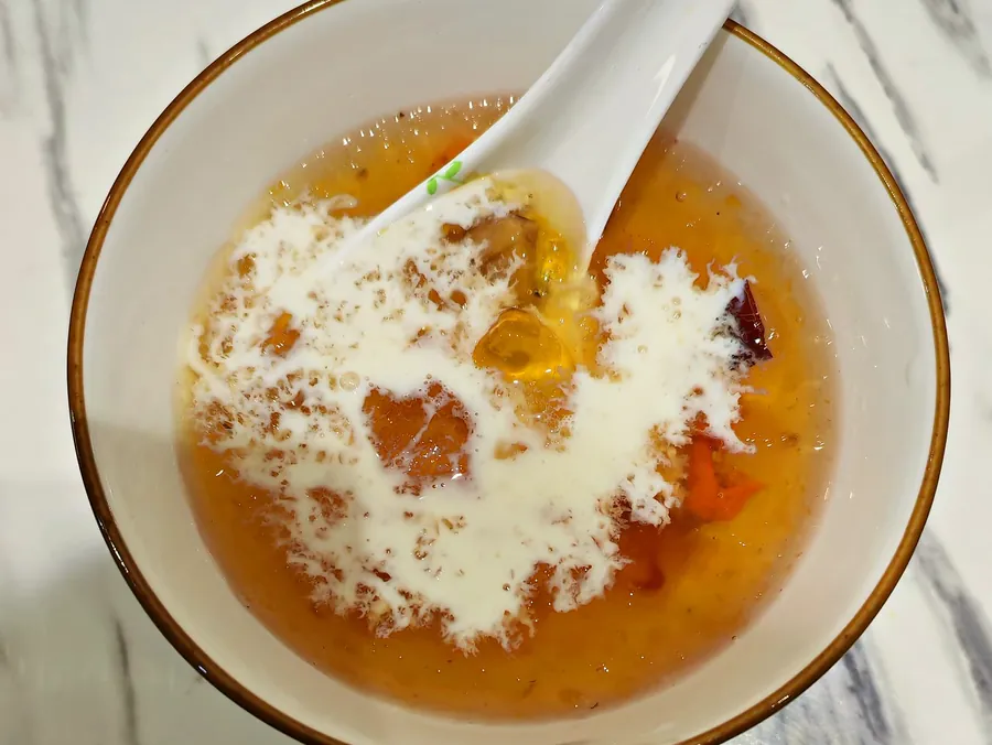 白碗里的桃胶雪燕牛奶,牛奶刚淋在金黄的桃胶上,白色汤匙放在碗里,俯拍。